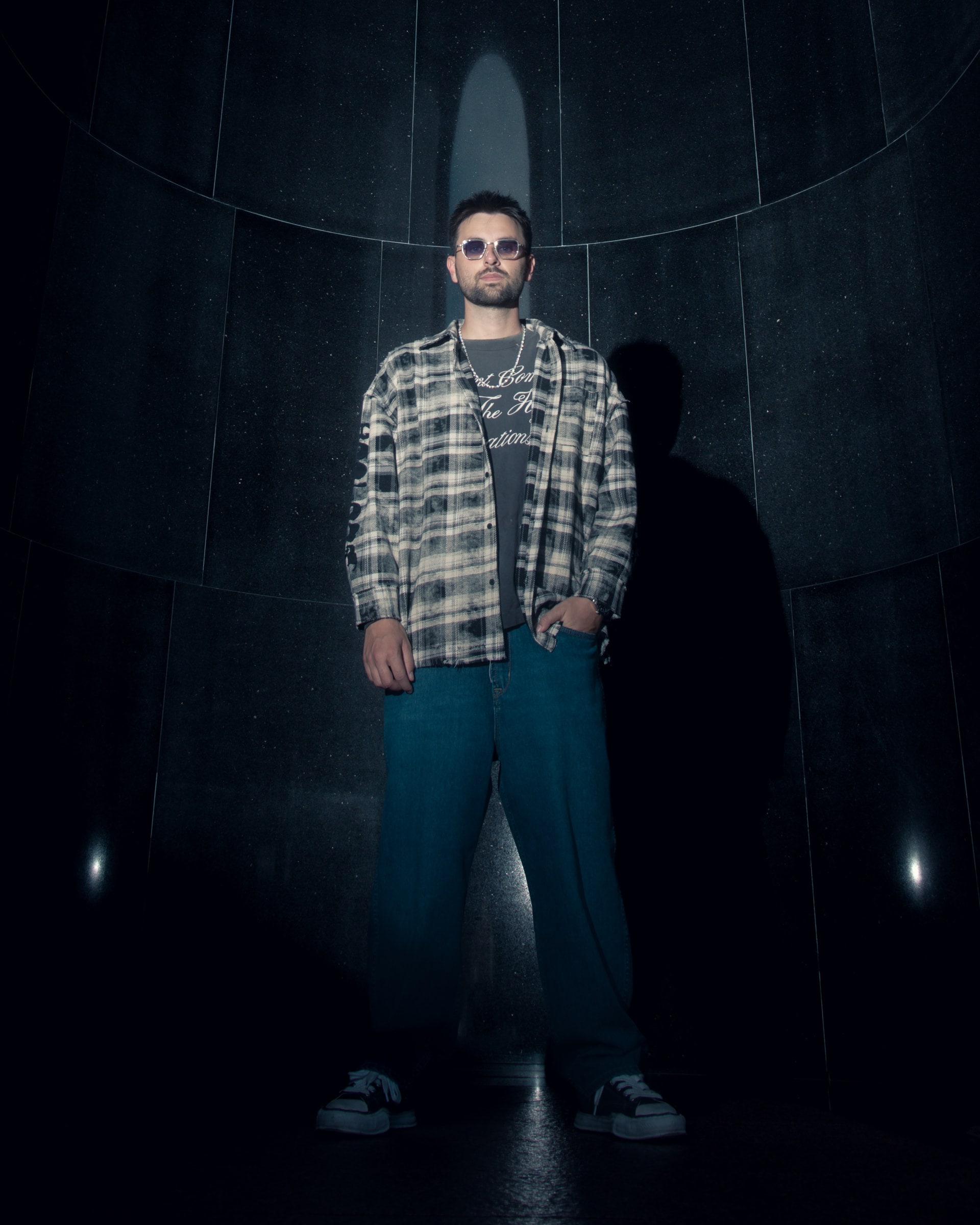 GATANO standing in a dark curved chamber, lit from above by a single cold spotlight.